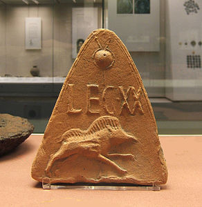 une tuile de céramique triangulaire portant l'inscription « LEGXX » au-dessus d'un sanglier courant