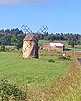 Windmühle aus Stein auf Hochebene mit Bauernhaus im Hintergrund