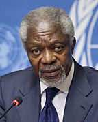 Photographie de Kofi Annan en 2012, représentant de l'Organisation des Nations unies, un homme de couleur de peau noire, aux cheveux et à la barbe blanche, portant un costume avec chemise blanche, veste et cravate bleues.