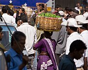 籠に野菜を満載し頭にのせて歩く女性。（インド、バンガロールのKRマーケット）