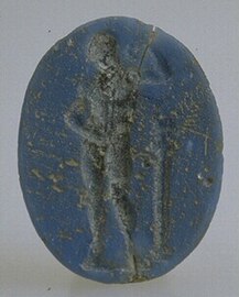 Intaille en verre bleu foncé, figurant un personnage. Le fond, légèrement surélevé, est pourvu de trois anneaux concentriques.