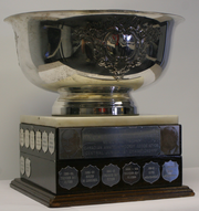 Wide and shallow ornate silver bowl mounted on a rectangular wooden base adorned with name plates