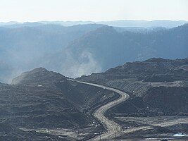 Mountaintop mining site with flattened land revealing dirt and mining roads in the foreground and unmined mountains in the background.