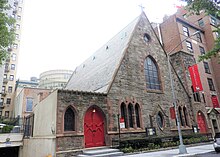 A brown stone triangular building with a square tower at the right on a city street. Its windows have pointed arches and there are similarly shaped red doors on either side. A large purple banner hanging from it has the word "Resurrection" on it