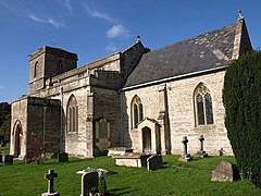 Stone building with square tower to left hand end. Foreground shows gravestones in grass area.