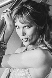 Photo en noir et blanc d'Amanda Lear, le bras gauche levé et sa main gauche placée près de sa tempe droite.