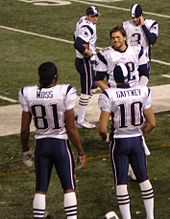 Cinq joueurs de football américains habillés de maillots blancs au bord d'un terrain de football américain.