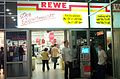 Außen alt, innen neu: Der inzwischen geschlossene Rewe-Markt im Friedrich-List-Platz 2, Dresden, im Oktober 2006. Während innen das Design auf die „neue REWE“ angepasst wurde, ist davor noch das alte „REWE-Korbband“-Logo angebracht.