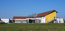 Un bâtiment à étage jaune et un bâtiment de plain-pied blanc encadrant une cours de récréation.