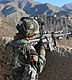 An Afghan National Army soldier in camouflage gear points a rifle over a dirt wall