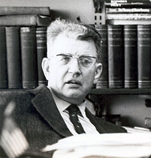 Coase looking to the camera and smiling, wearing a suit and tie