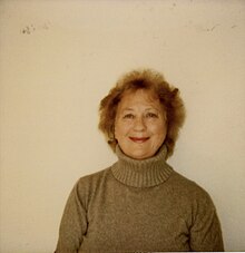 Polaroid of older woman smiling in light grey polar neck jumper.