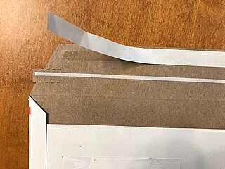 Paperboard mailing envelope showing PSA adhesive with release liner and with tear tape