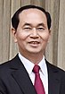 a smiling man with black hair, dressed in a suit with an pink tie