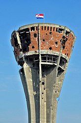 A severely damaged brick and concrete tower, pierced with numerous shell holes