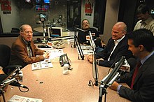 Several people around a table with microphones in a radio studio