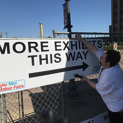 A volunteer hangs signage in preparation for the Mini Maker Faire in Tyler, Texas (April 2019) Image: Paul Budd.