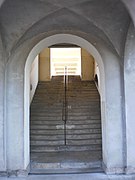Vu du bas, traversant un bâtiment, un escalier de pierre séparé dans sa longueur par une rambarde en fer ; on y accède par un porche cintré, en haut l'ouverture est rectangulaire.