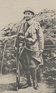 Une femme déguisée en poilu, arme à la main, dans les tranchées de la Première Guerre mondiale.