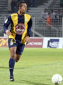 Photographie d'un joueur de football, avec un maillot jaune et noir, qui court et qui regarde à sa gauche.