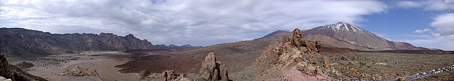 Parois rocheuses de la caldeira à gauche, le volcan à droite et des formations rocheuses avec de nombreux touristes au premier plan.