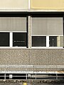 Unterschiedliche, physische Texturen bei einer Architektur. Detail einer Vorhangfassade aus Betonsockel, Glas (Fenster), Sonnenschutzrollos und gelblichem Metall.