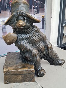 A bronze statue of Paddington Bear. Paddington wears a hat, has a label around his neck and sits on a suitcase.