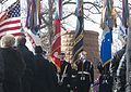 Photo de plusieurs personnes tenant des drapeaux devant le monument vertical composé de pierres. Des personnes se tiennent de chaque côté et assistent à la cérémonie.