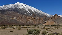 Sommet enneigé du volcan en arrière-plan, avec une zone plate désertique au premier-plan.