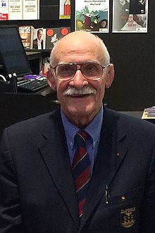 Un homme avec des lunettes, une moustache et en costume cravate.
