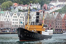 Fier petit bateau à moteur en parade dans un bassin maritime devant une belle rangée de maisons de ville.