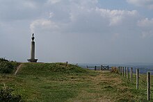un monument en forme d'obélisque se dresse sur un terre-plein herbeux au sommet d'une colline.