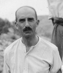 Black-and-white photograph of a moustachioed man, facing the camera, with an open-necked shirt.