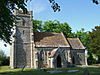 Stone building with square tower, surrounded by trees.