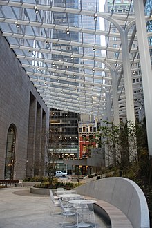 Southward view of 550 Madison Garden, the building's renovated atrium, in 2022. The atrium has a glass roof. On the left is the building's facade, while on the right are benches and plants.