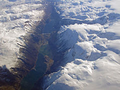 Aerial view, looking south. The fjord is on the bottom of the picture, then the town, then the lake Sandvinvatnet at the top. The snow-covered mountains surround the town.