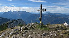 Une croix chrétienne en bois au sommet d'une montagne caillouteuse et à l'herbe rase.