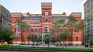 The Park Avenue Armory as seen from Park Avenue in 2019. The armory has a brick facade and a tower rising above the center of the building.