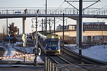 Yellow and blue light rail train travels across a grade crossing