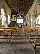 Photo d'un intérieur d'église, où l'on voit la nef couverte par une charpente lambrissée, des arcades sur les côtés et le chevet percé par un grand vitrail