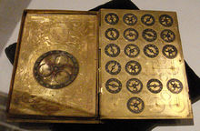 book sized metal machine with large dial left page and nineteen small dials right page