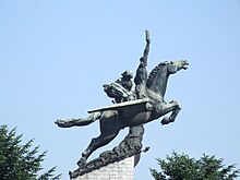 Statue d'un cheval au galop, portant deux personnes sur son dos, sur une colonne