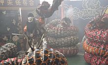 Acteur se mouvant au milieu de têtes de dragon de papier dans une atmosphère enfumée.