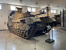 Tracked armoured vehicle with gun barrel and turret in situ inside a large museum gallery.