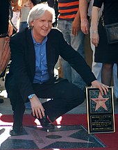 director James Cameron squats by his new star, left hand propping up his plaque