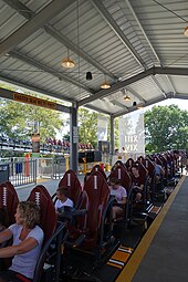 Riders sitting on the roller coaster within the ride's station. The seats are themed to American football, with a white stripe on a brown background.