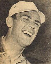 Portrait en noir et blanc d'un homme qui sourit et qui porte une casquette blanche.