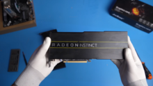 Two glove-covered hands hold AMD Radeon Instinct MI50 card. The background is unsharp.