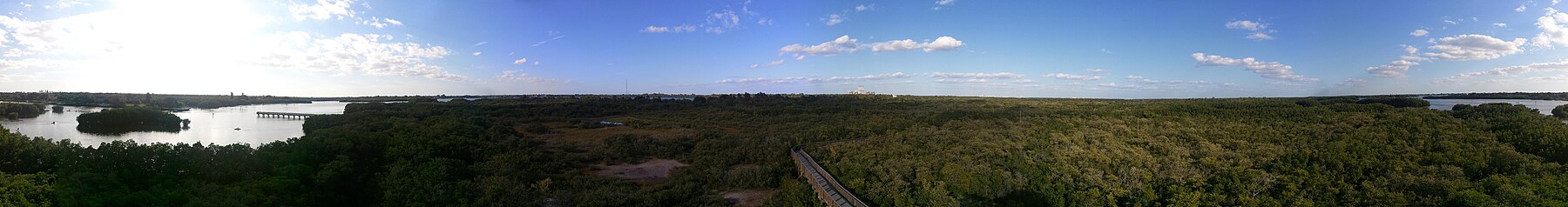 Panorama of mostly scrubby swamp, with various buildings/structures visible on the horizon.