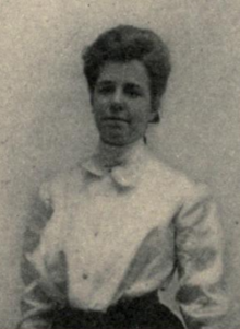 A young white woman with dark hair in an updo, wearing a white button-down blouse